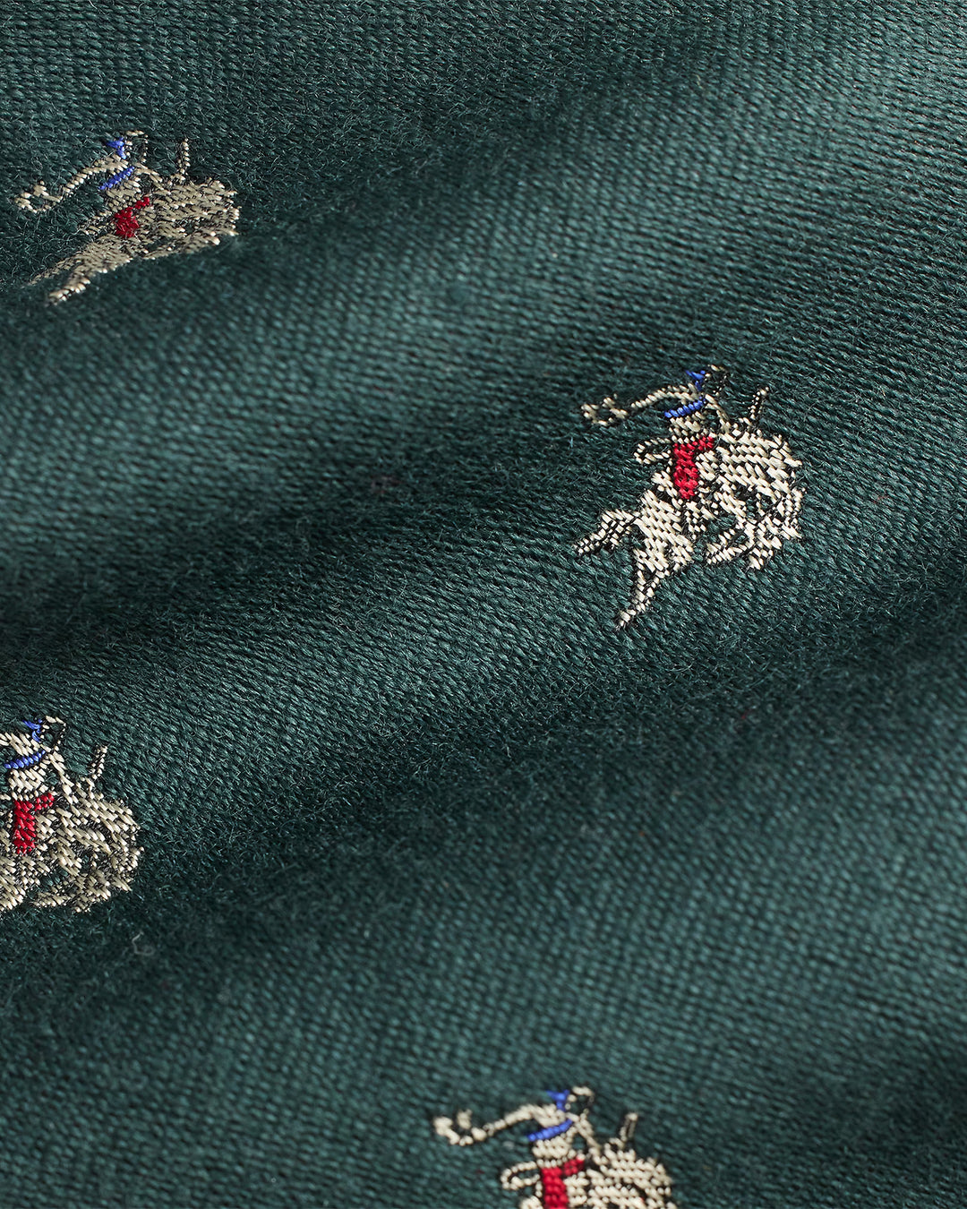 Dark green fabric with embroidered patterns of figures on horses.
