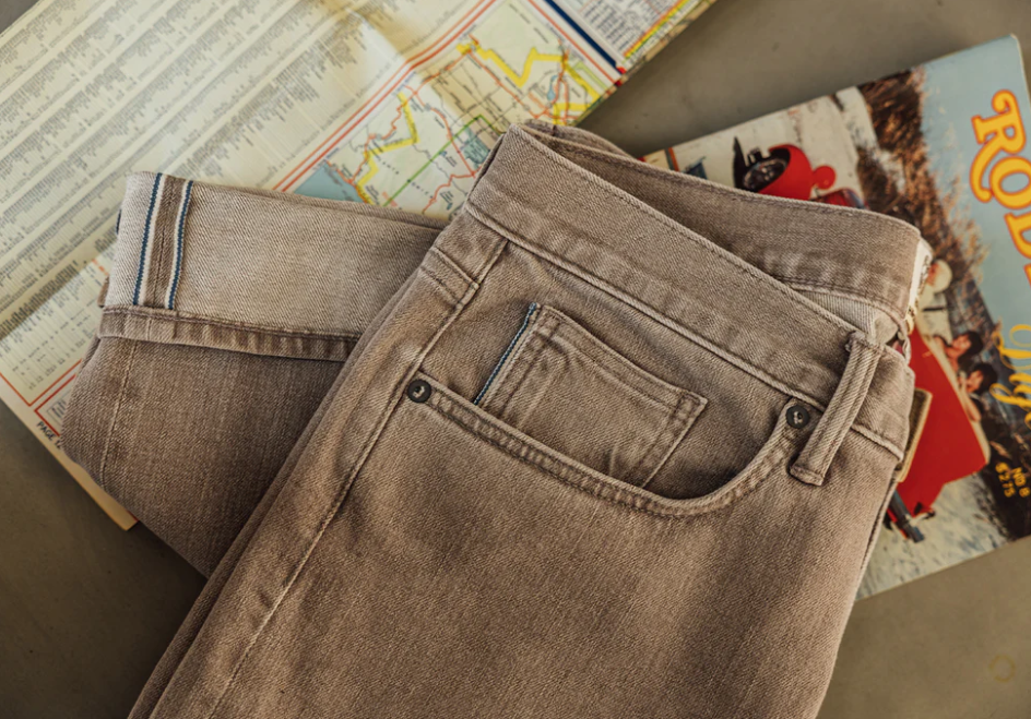 Folded brown jeans on top of vintage books and maps