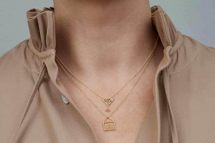 Gold necklace with a pendant worn by a person in a beige shirt against a neutral background