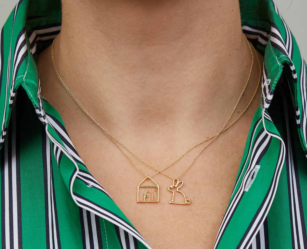 Gold necklace with house and rabbit pendant worn by a person in a green striped shirt.