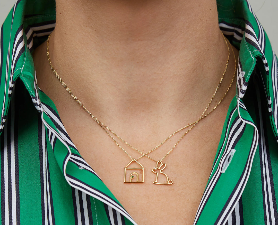 Gold necklace with house and rabbit pendant worn by a person in a green striped shirt.