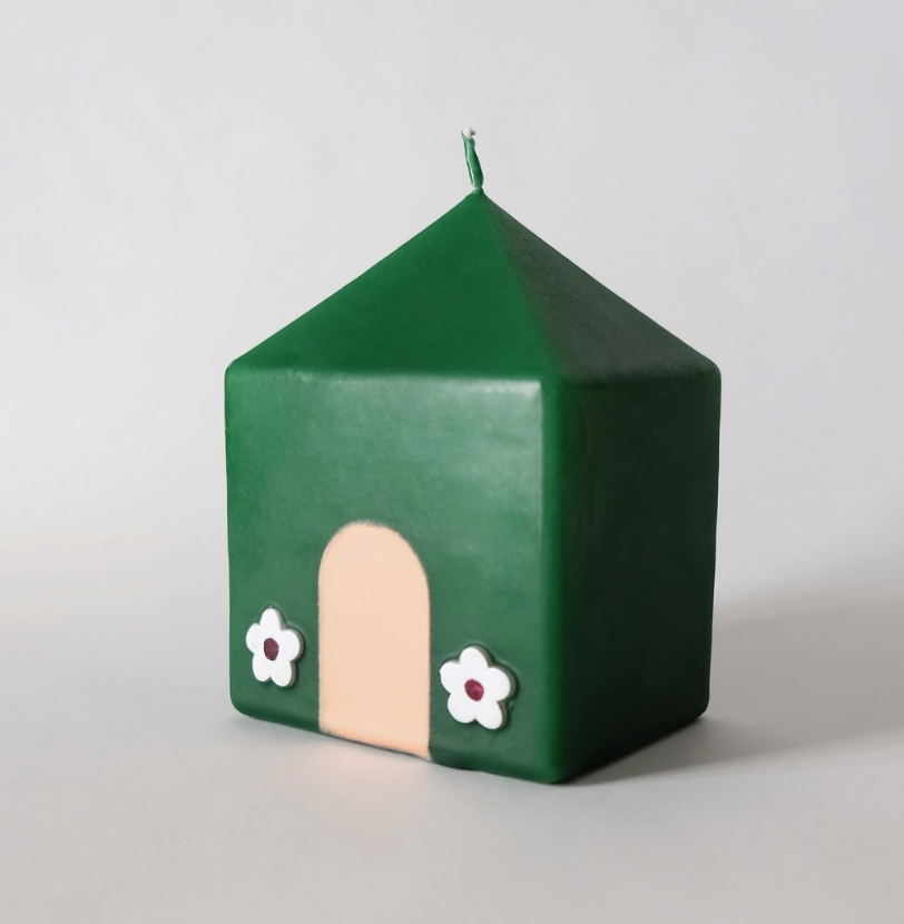 Green candle shaped like a house with a beige door and white flowers on a light gray background