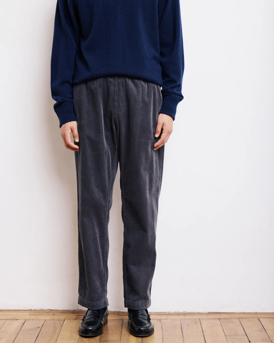 Person wearing a navy sweater and gray pants against a white wall.