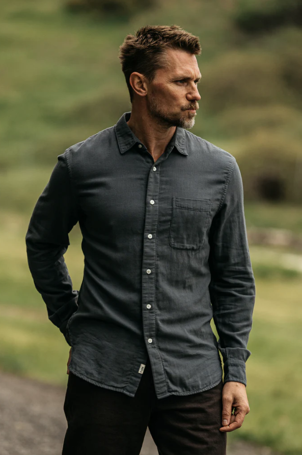 Man wearing a dark gray shirt standing outdoors with a blurred natural background