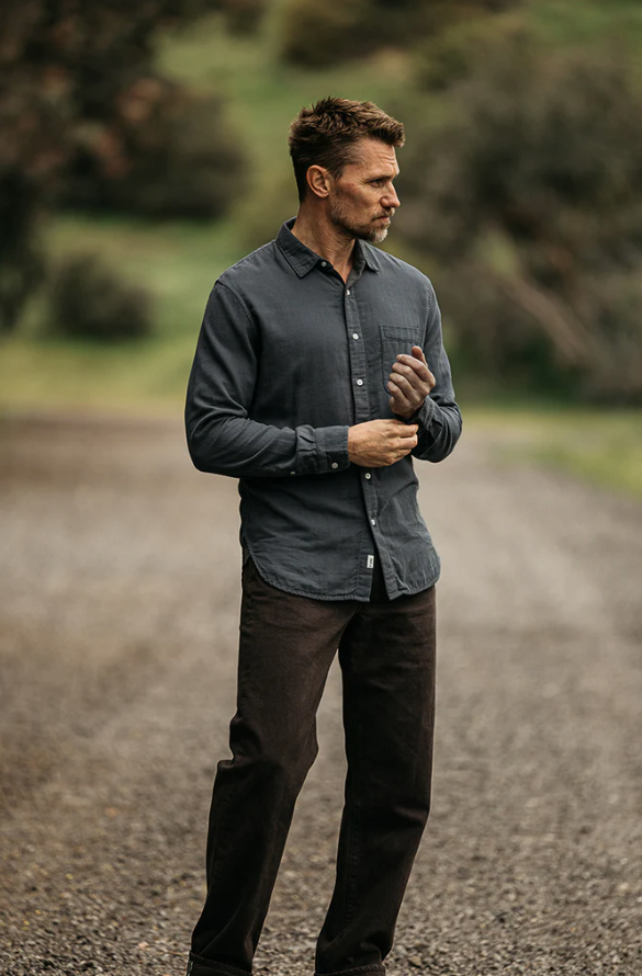 Man wearing a dark shirt and pants standing on a gravel path with greenery in the background