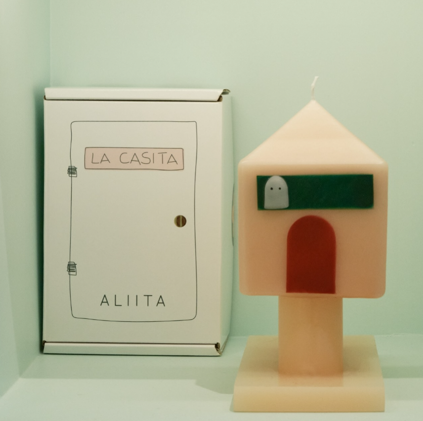 House-shaped candle next to its packaging with 'LA CASITA' branding on a light green background