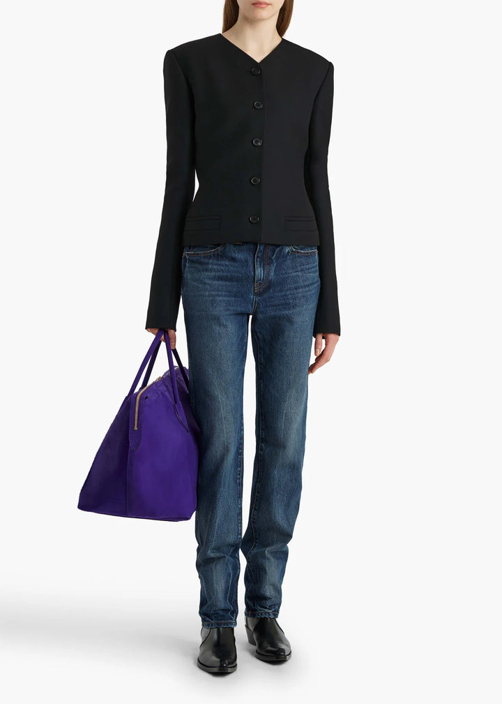 Person wearing a black cardigan, blue jeans, and holding a purple bag on a white background