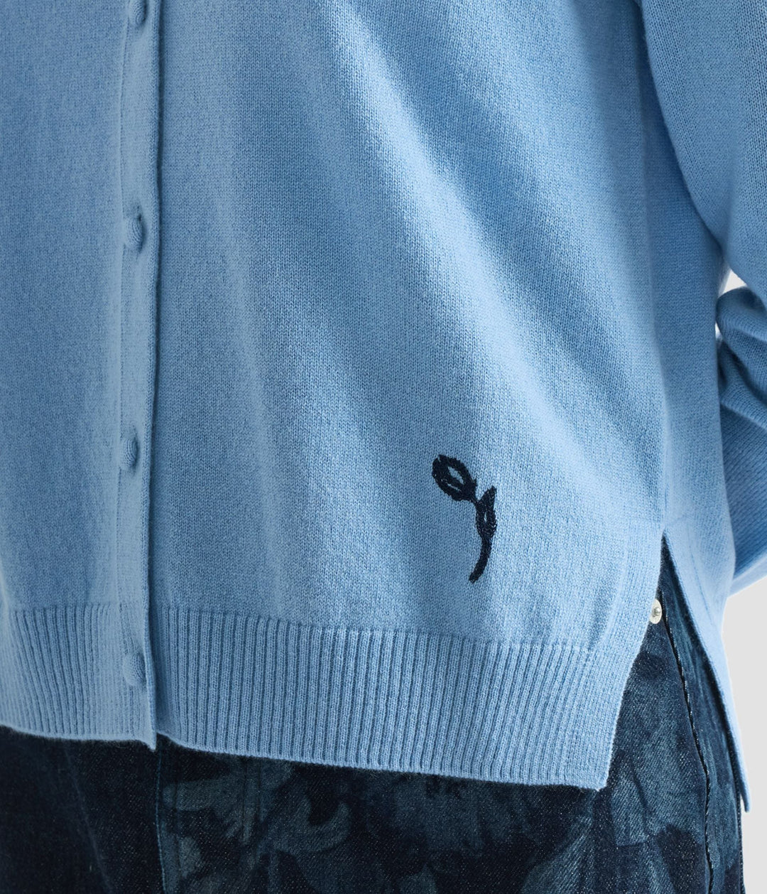 Light blue cardigan with a black embroidered design on a neutral background