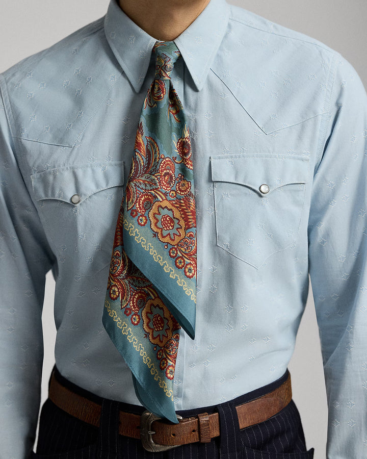 Light blue shirt with a patterned tie and brown belt on a plain background