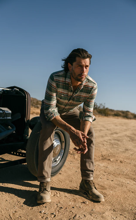 Man sitting on a dirt road next to an open car door with a clear blue sky.