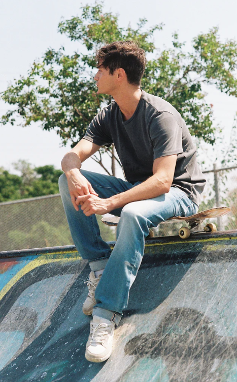 Man sitting on a skateboard at a skate park with trees in the background