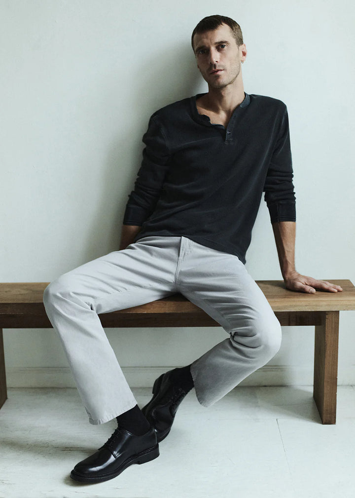 Man sitting on a wooden bench wearing a black shirt, light gray pants, and black shoes.