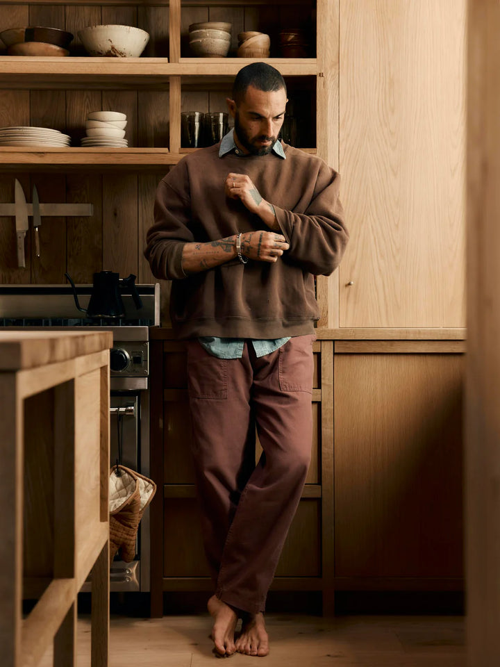 Man standing in a kitchen wearing a brown sweater and pants.