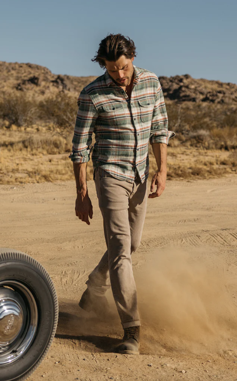 Man walking on a dirt road with a tire nearby, desert landscape in the background