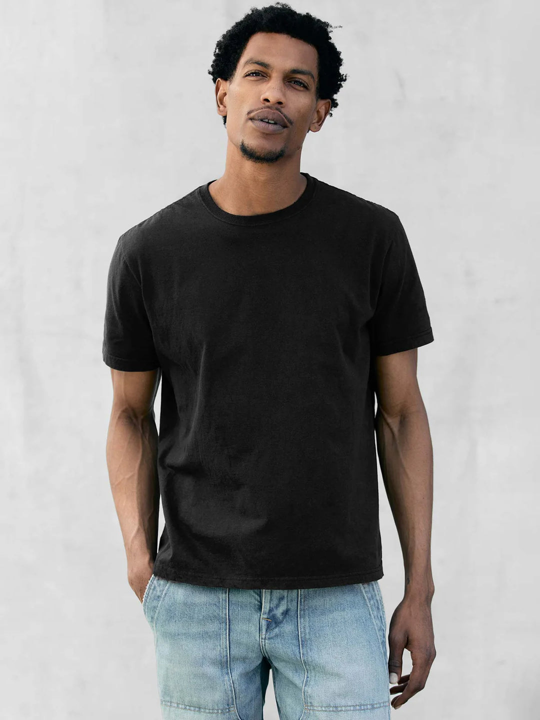Man wearing a black t-shirt and light blue jeans against a white background