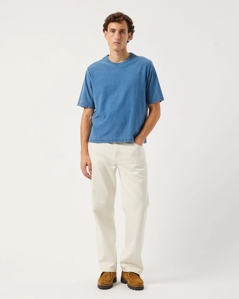 Man wearing a blue t-shirt and white pants on a white background