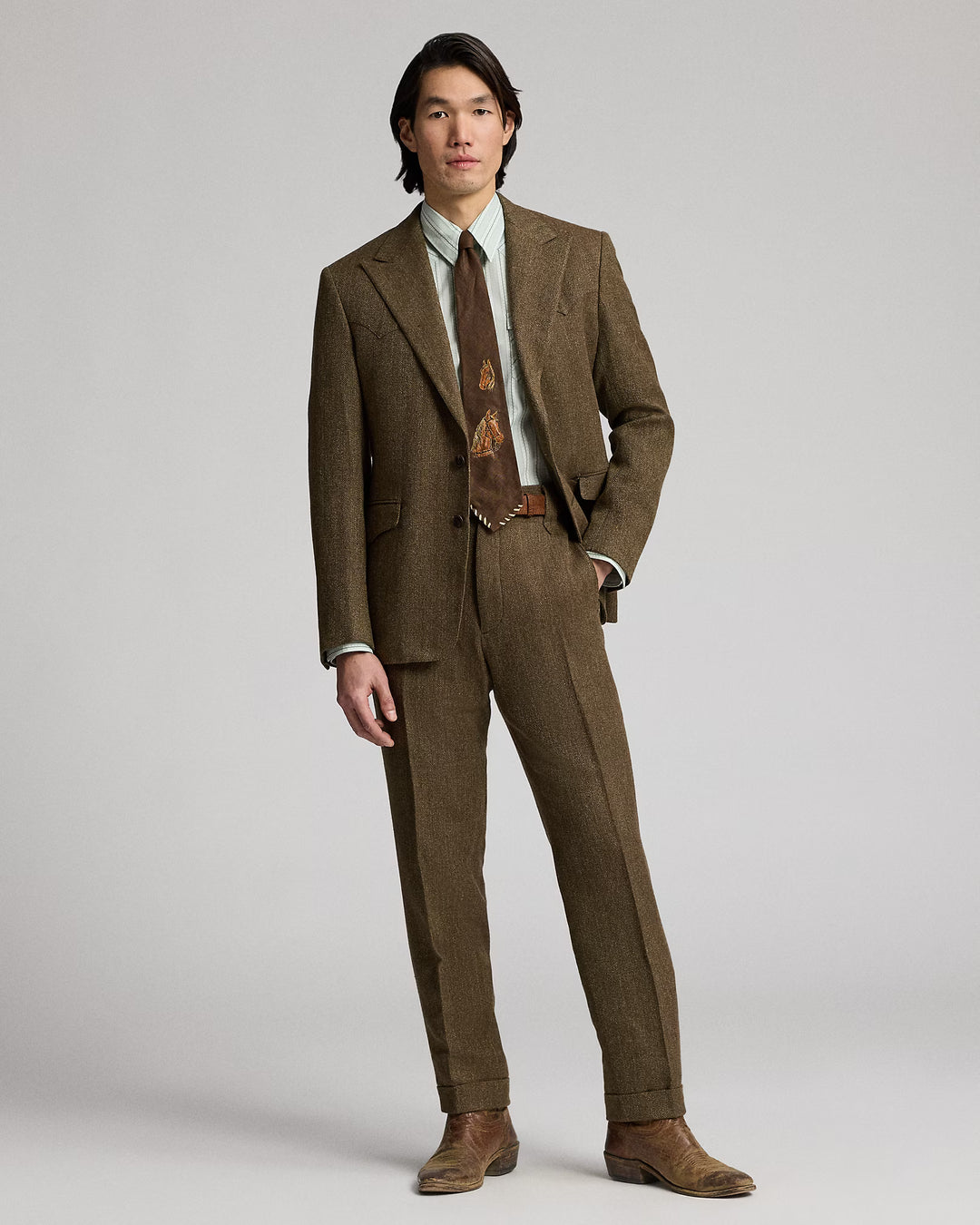 Man wearing a brown suit with a patterned tie on a plain background