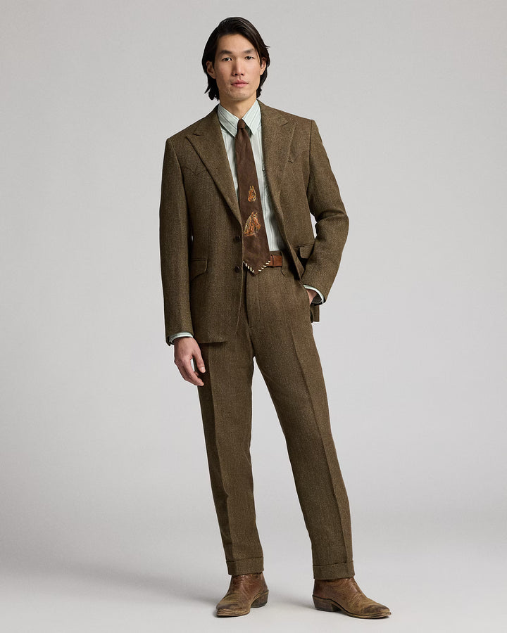 Man wearing a brown suit with a patterned tie on a plain background