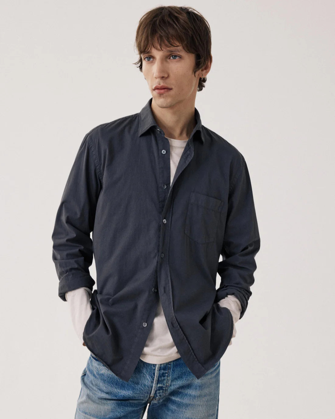 Man wearing a dark blue shirt over a white shirt with blue jeans on a light gray background