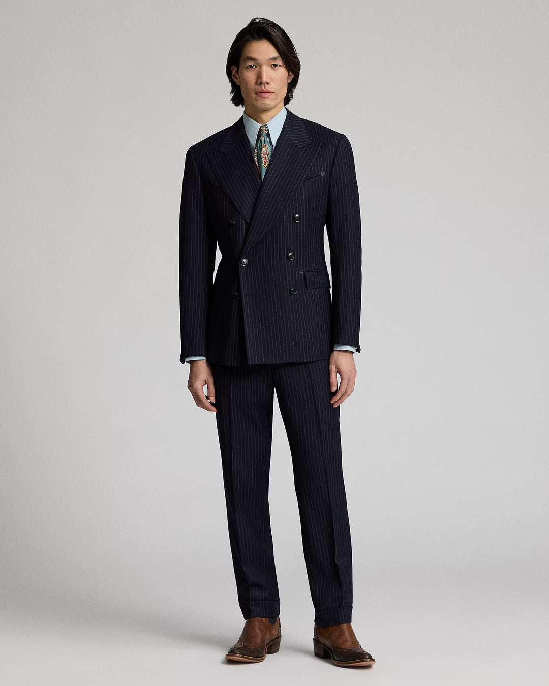 Man wearing a dark pinstripe suit with a white shirt and patterned tie on a light gray background