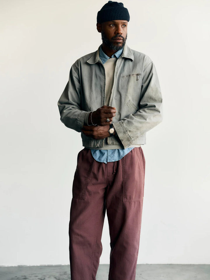 Man wearing a gray jacket, blue shirt, and maroon pants against a white background
