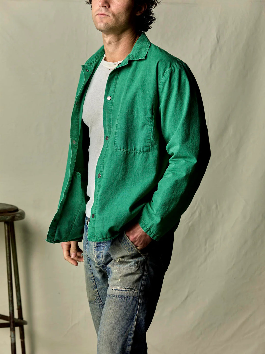 Man wearing a green jacket over a white shirt and jeans against a plain background