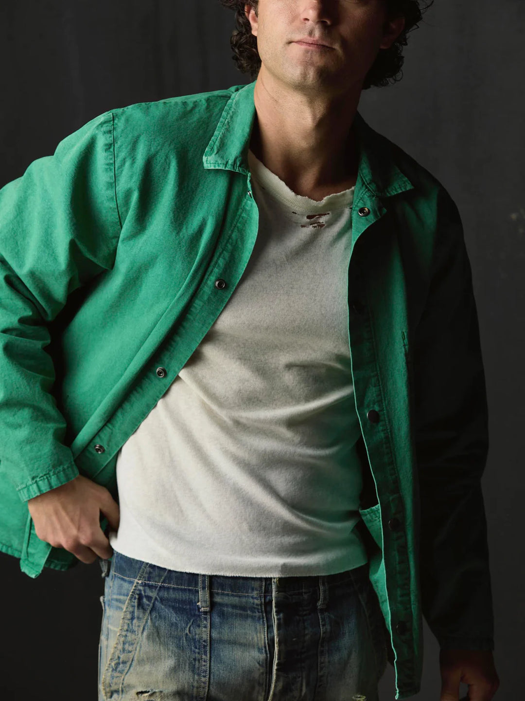 Man wearing a green jacket over a white shirt with a dark background