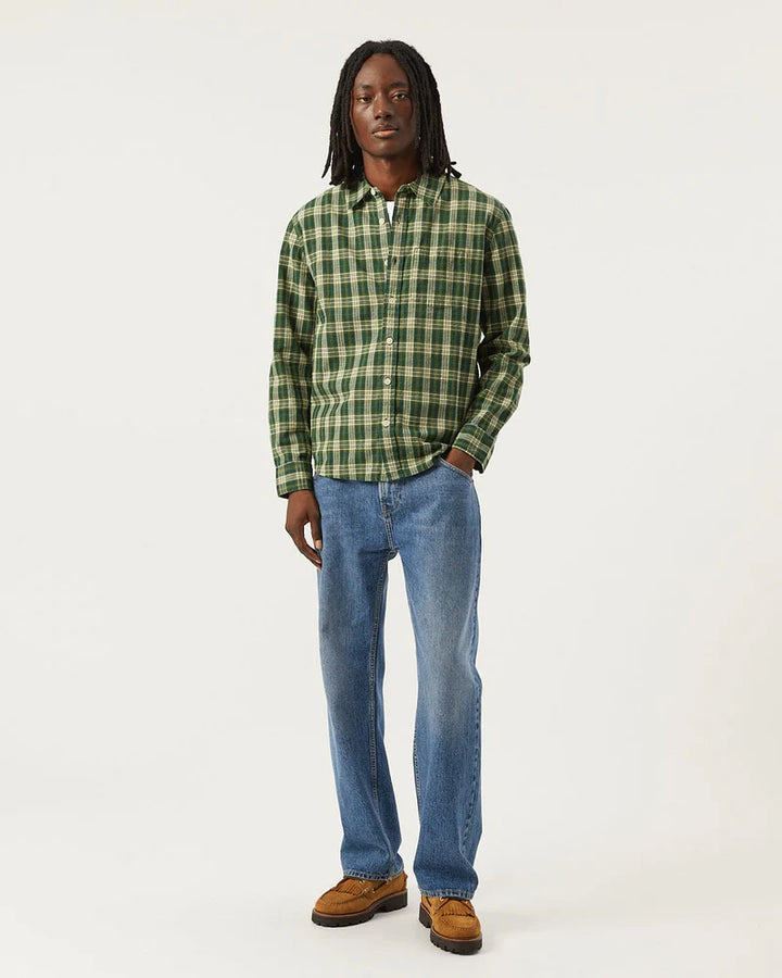 Man wearing a green plaid shirt, blue jeans, and brown shoes on a white background