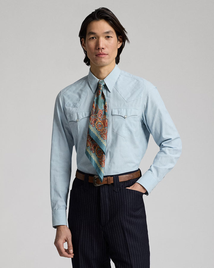 Man wearing a light blue shirt with a patterned tie and dark pants on a gray background