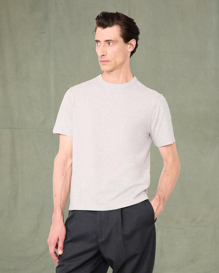 Man wearing a light gray t-shirt and dark pants against a green background