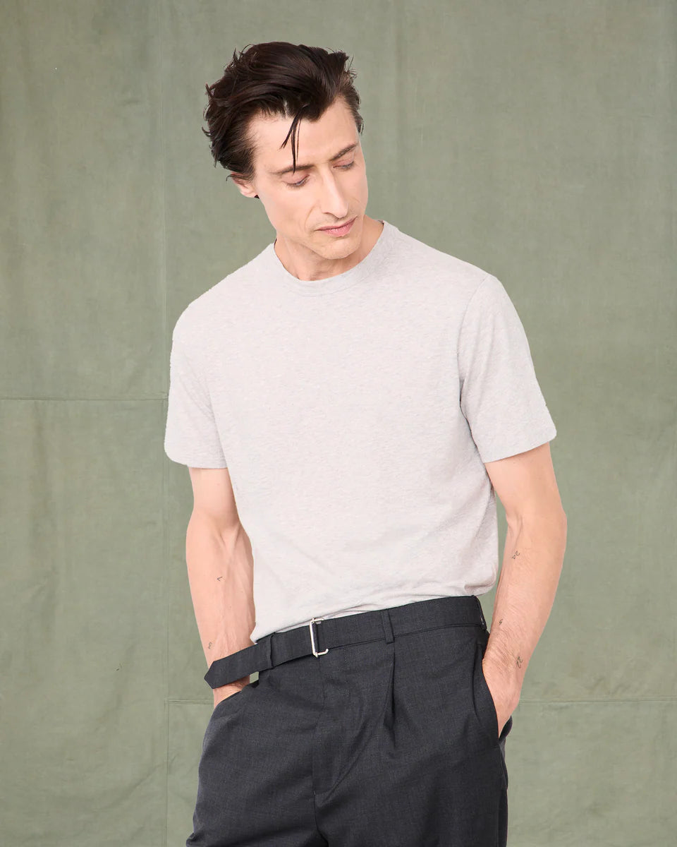 Man wearing a light gray t-shirt and dark pants against a plain background