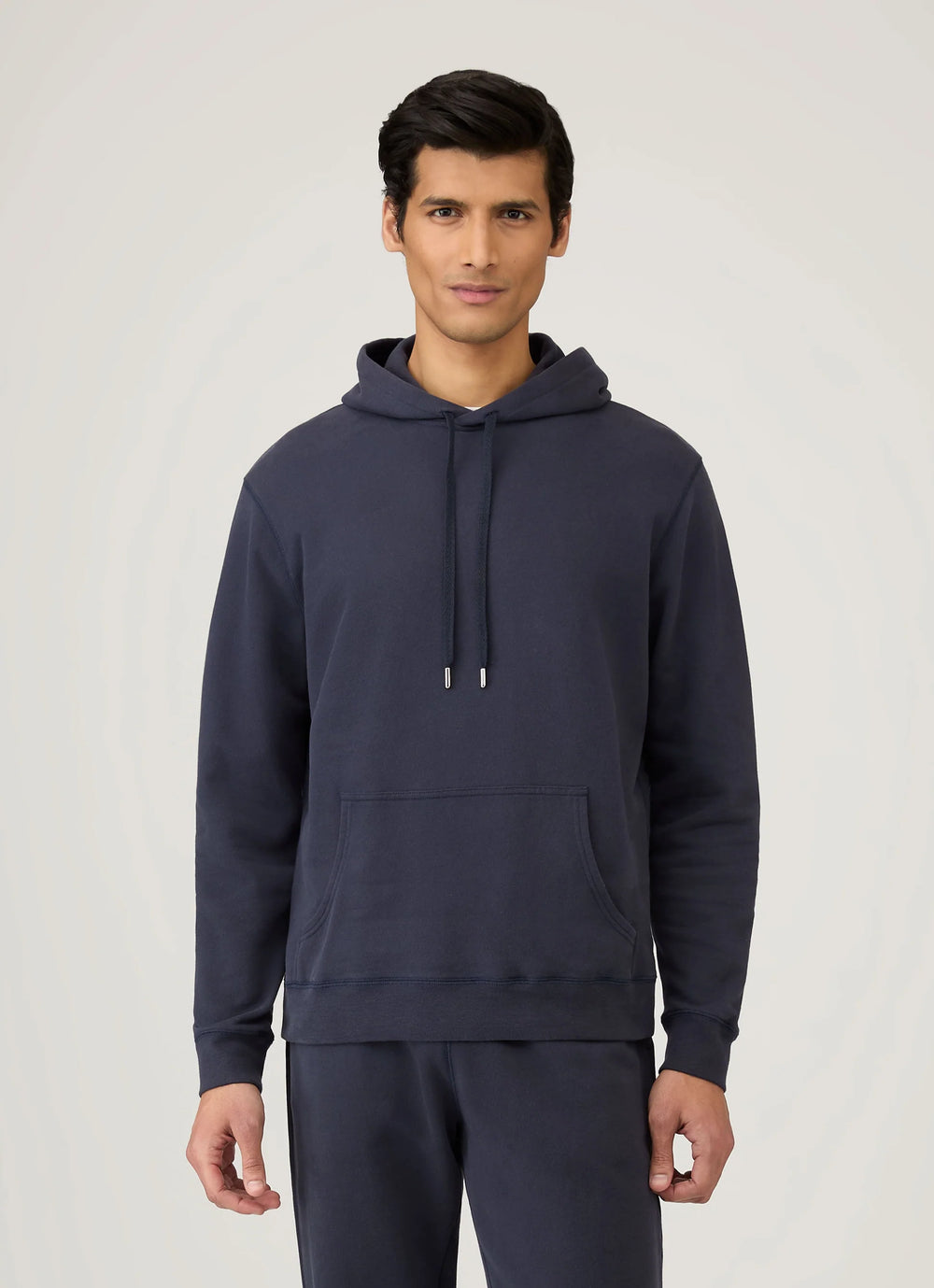 Man wearing a navy blue hoodie and pants on a light gray background