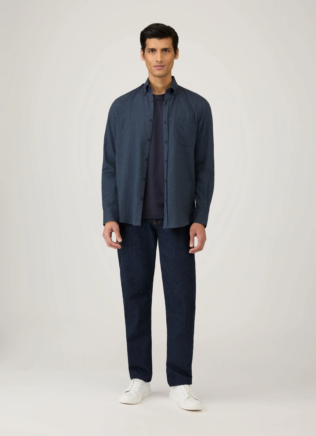 Man wearing a navy jacket, shirt, and pants with white shoes on a light gray background