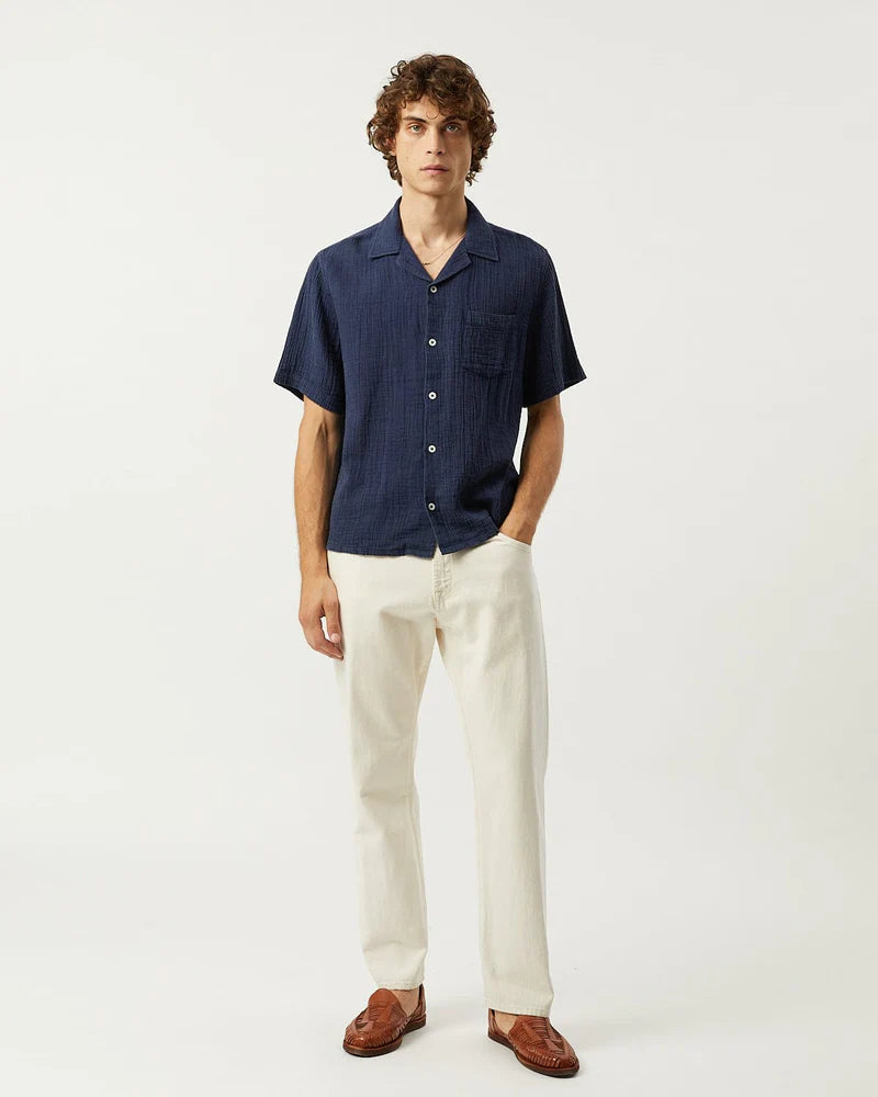 Man wearing a navy short-sleeve shirt and white pants on a white background