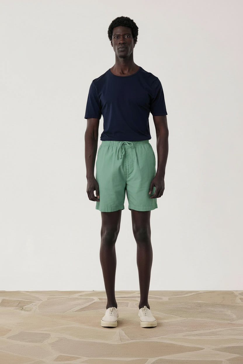 Man wearing a navy t-shirt and blue shorts standing against a plain white background