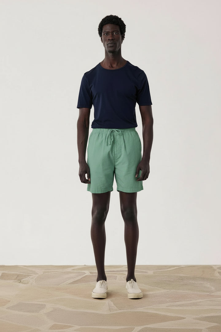 Man wearing a navy t-shirt and blue shorts standing against a plain white background