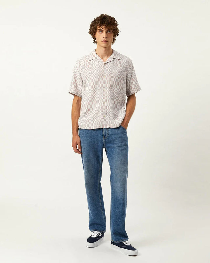 Man wearing a patterned shirt and blue jeans on a white background