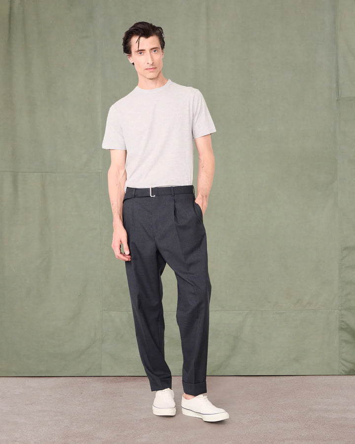 Man wearing a white t-shirt and dark pants standing against a green background