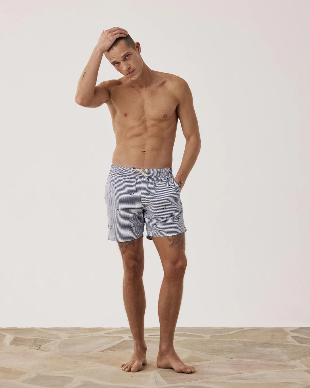 Man wearing gray swim shorts standing against a plain background