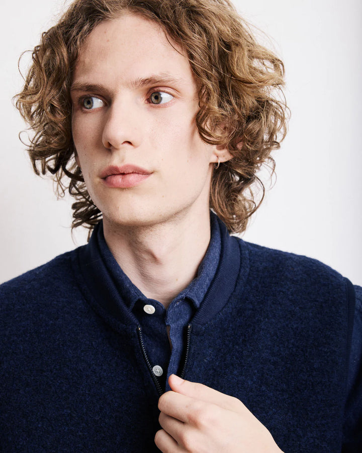 Man with curly hair wearing a navy blue jacket against a white background