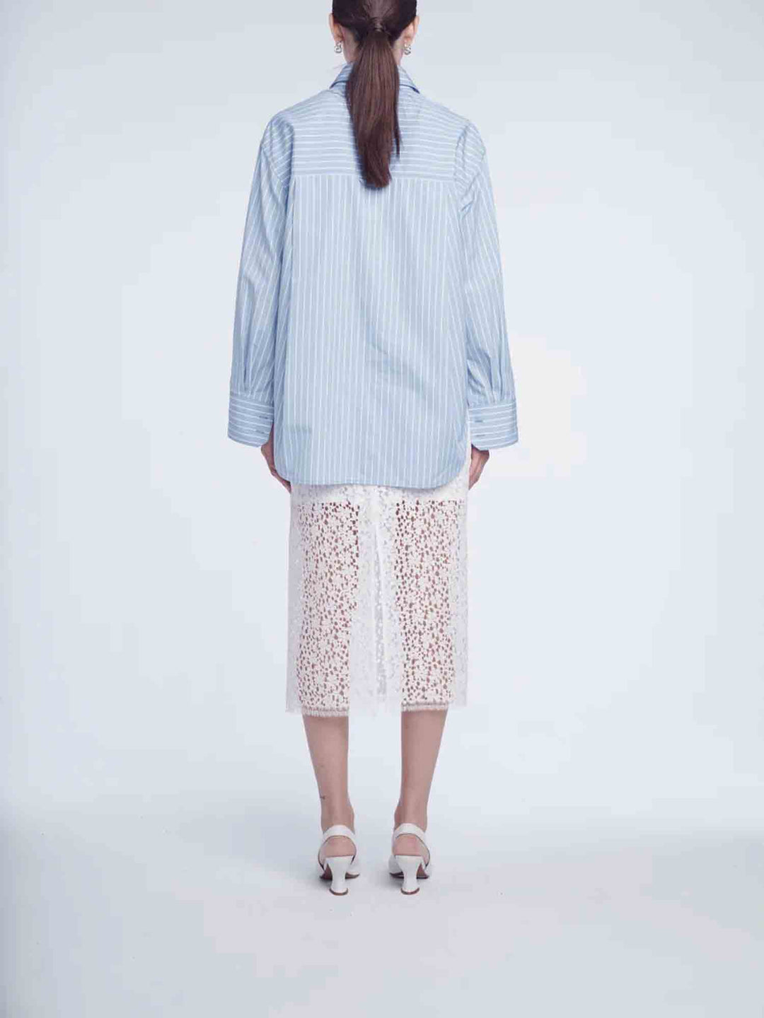 Person wearing a light blue striped shirt and white lace pants on a white background