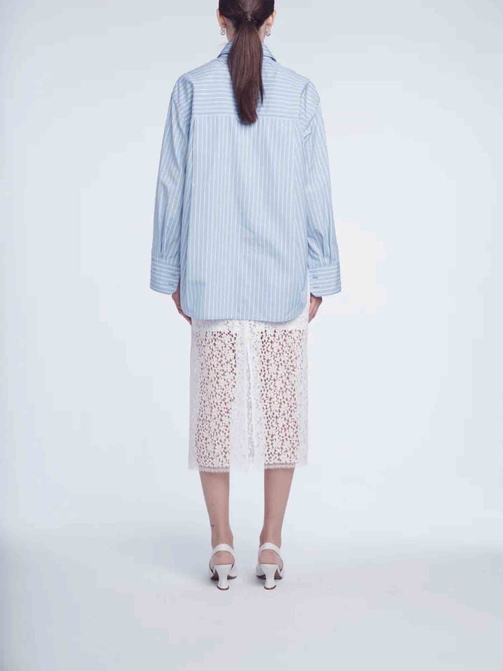 Person wearing a light blue striped shirt and white lace pants on a white background