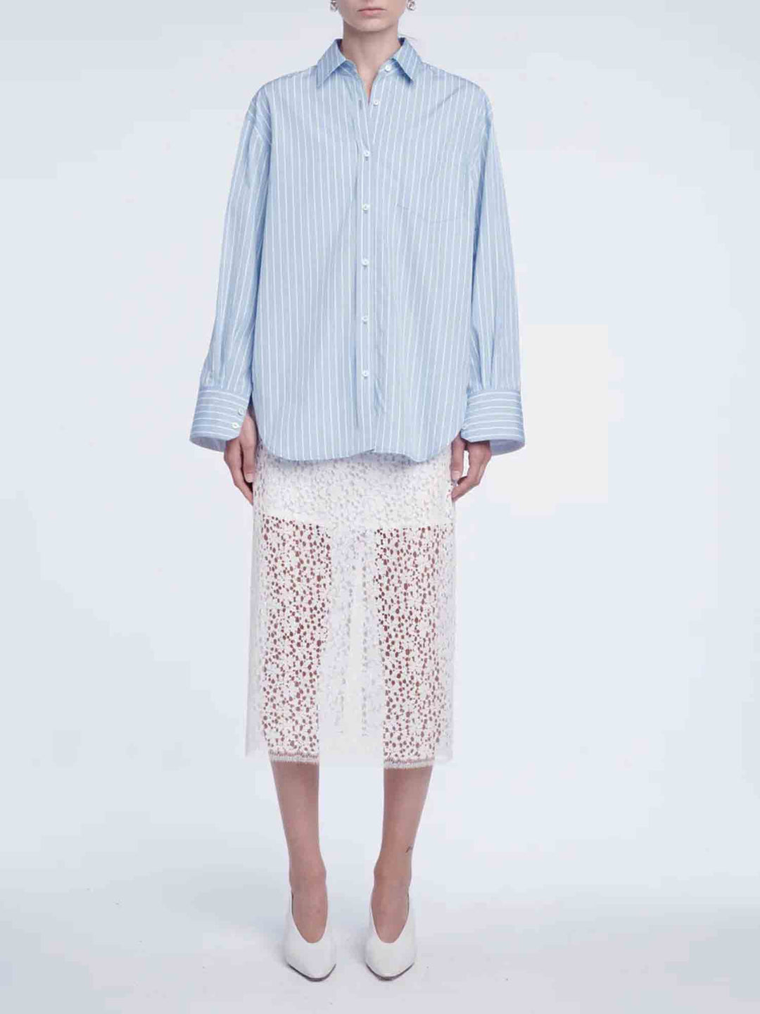 Person wearing a light blue striped shirt and white lace skirt on a plain background