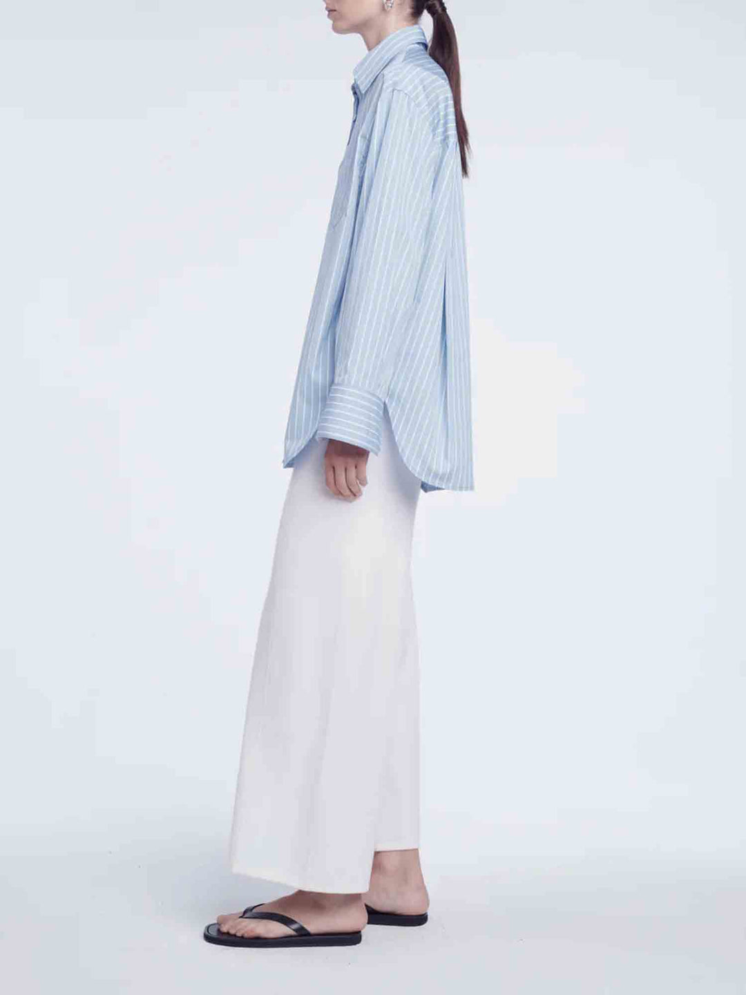 Person wearing a light blue striped shirt and white pants on a plain background