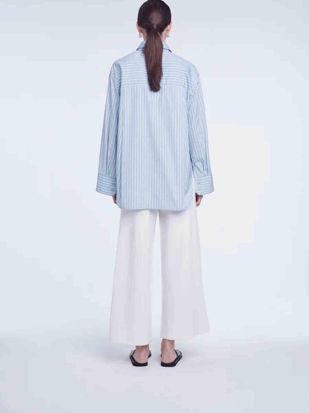 Person wearing a light blue striped shirt and white pants on a white background