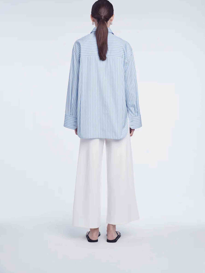 Person wearing a light blue striped shirt and white pants on a white background