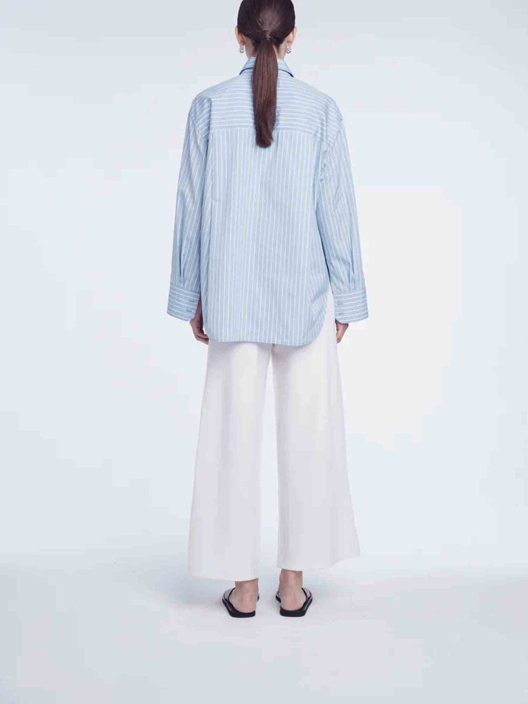 Person wearing a light blue striped shirt and white pants on a white background