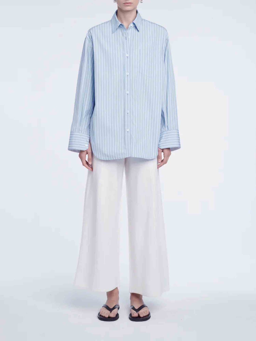Person wearing a light blue striped shirt and white pants on a white background
