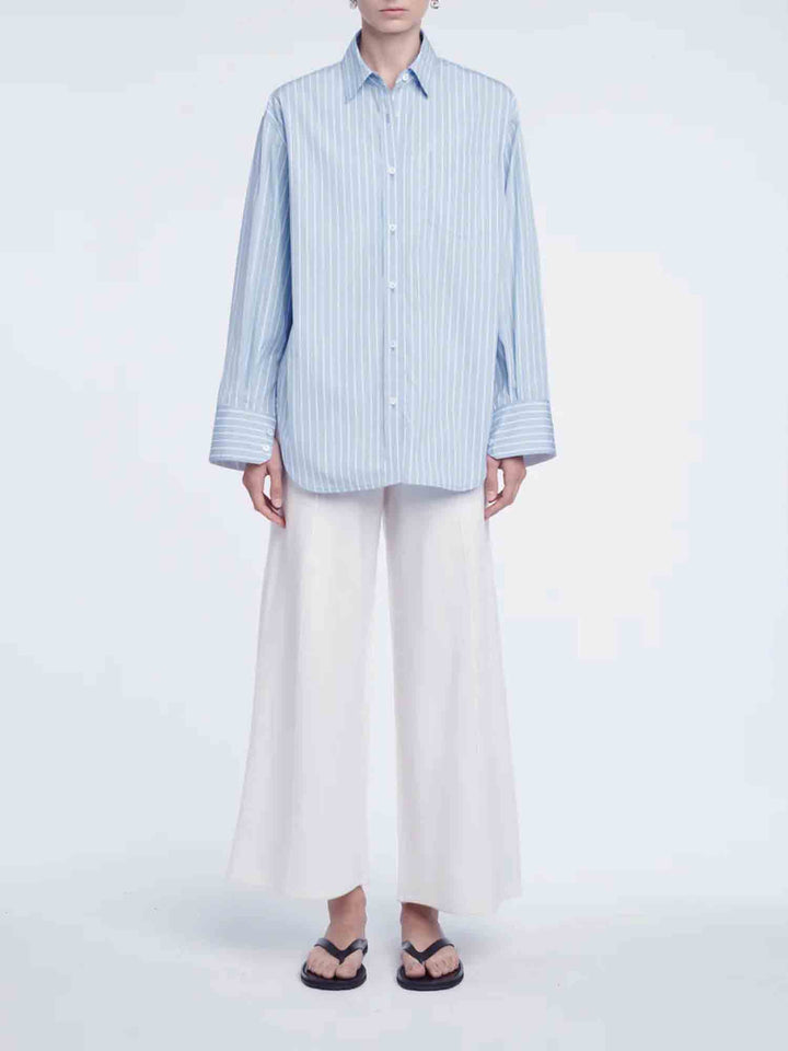 Person wearing a light blue striped shirt and white pants on a white background