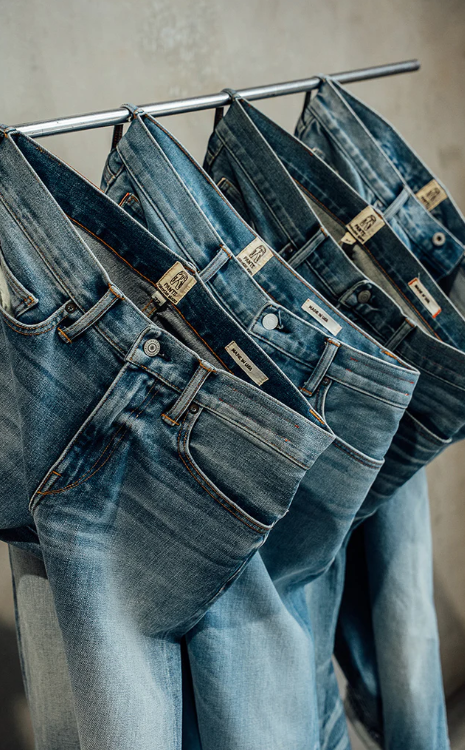 Multiple pairs of blue jeans hanging on a rack with visible brand labels.